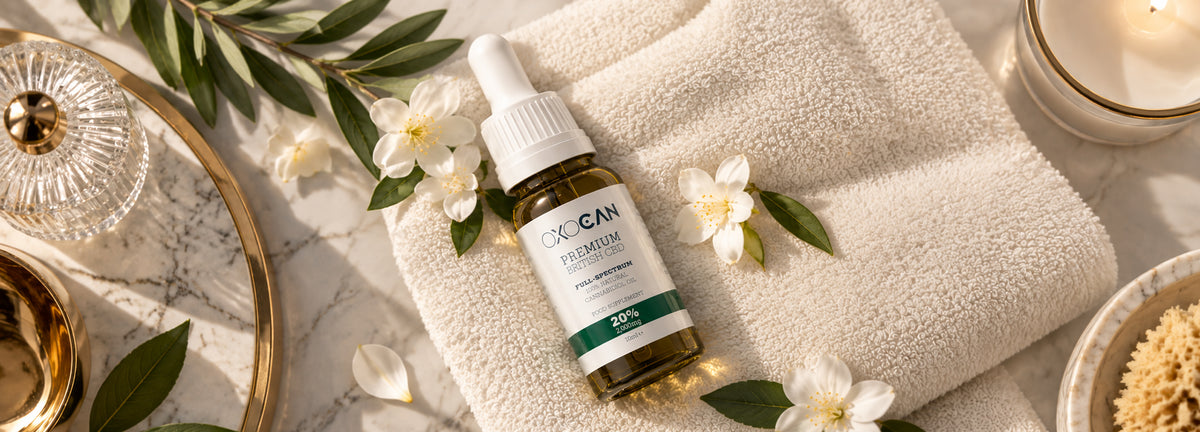 Oxocan full-spectrum CBD oil bottle styled with white spa towels and elegant marble and gold accessories.